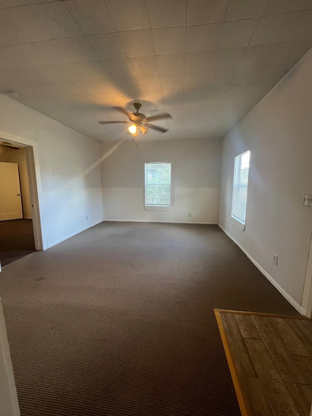 empty room featuring dark carpet, a ceiling fan, and baseboards