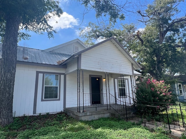 view of front facade featuring covered porch, metal roof, and fence