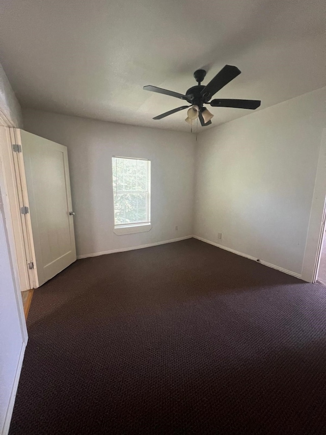 empty room with baseboards, dark carpet, and a ceiling fan