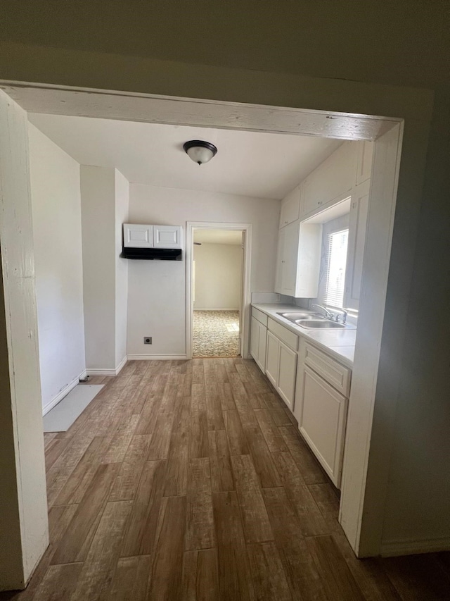 kitchen featuring dark wood finished floors, light countertops, white cabinetry, a sink, and baseboards