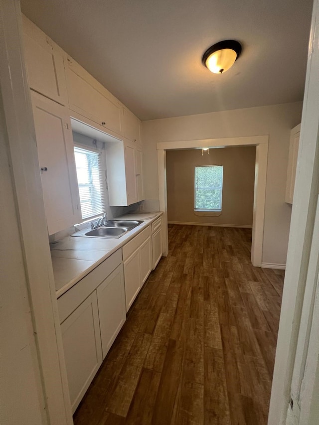 kitchen featuring baseboards, white cabinetry, dark wood-type flooring, and a sink