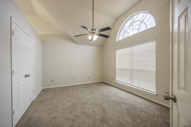 interior space with a textured ceiling, carpet flooring, a ceiling fan, baseboards, and vaulted ceiling