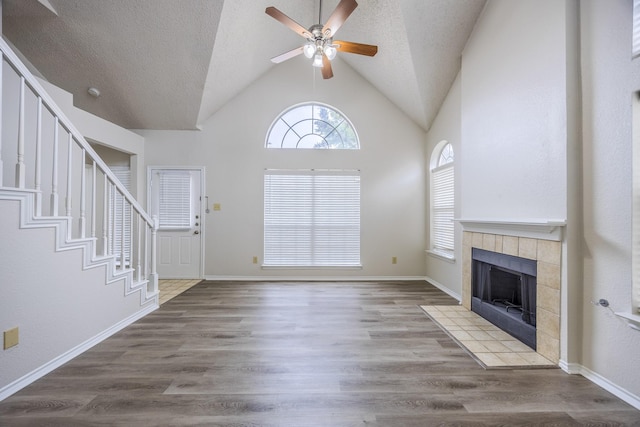 unfurnished living room featuring a ceiling fan, a tile fireplace, stairway, wood finished floors, and a textured ceiling