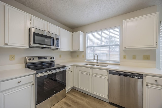 kitchen featuring light wood-style floors, appliances with stainless steel finishes, white cabinets, and a sink