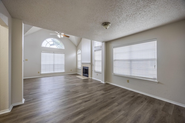 unfurnished living room with a tiled fireplace, ceiling fan, dark wood-style flooring, vaulted ceiling, and a textured ceiling