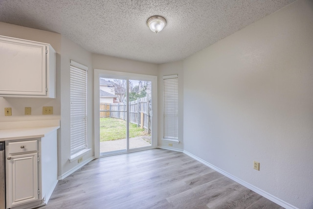 unfurnished dining area with light wood finished floors, baseboards, and a textured ceiling