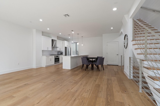 kitchen with visible vents, white cabinetry, appliances with stainless steel finishes, light wood-type flooring, and wall chimney exhaust hood