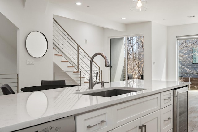 kitchen with wine cooler, a sink, light wood-style floors, white cabinets, and light stone countertops