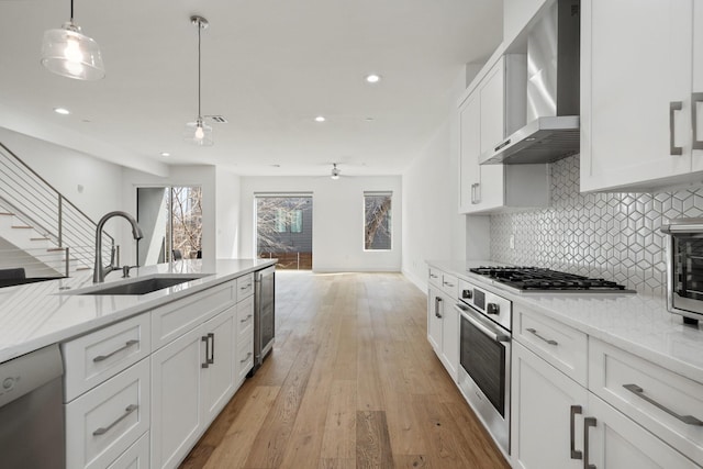 kitchen featuring beverage cooler, wall chimney exhaust hood, stainless steel appliances, white cabinetry, and a sink