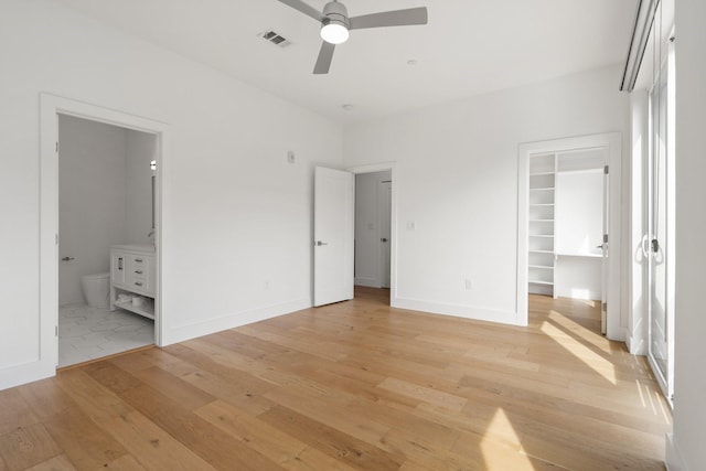 unfurnished bedroom featuring ensuite bathroom, light wood-style flooring, visible vents, baseboards, and a walk in closet