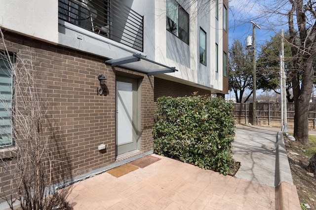 view of exterior entry featuring a patio area, fence, stucco siding, and brick siding