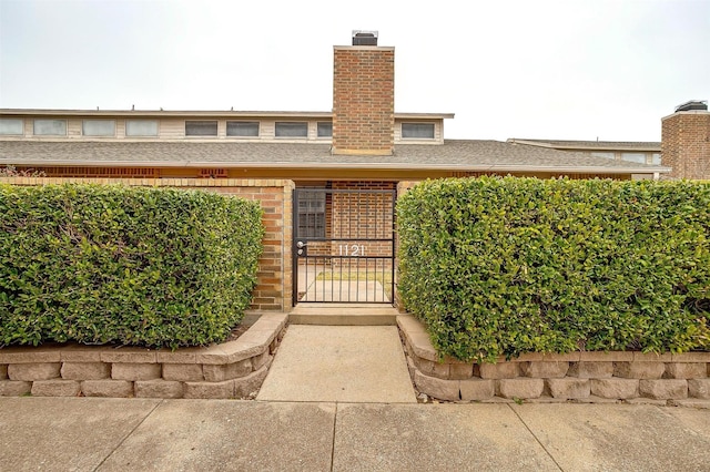 entrance to property featuring brick siding, a chimney, a shingled roof, and a gate