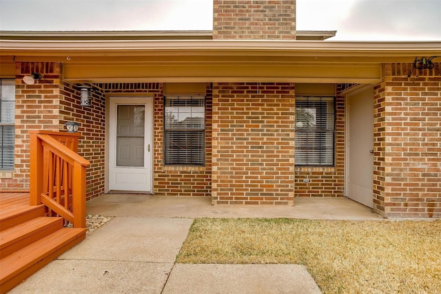 property entrance featuring covered porch, brick siding, and a chimney