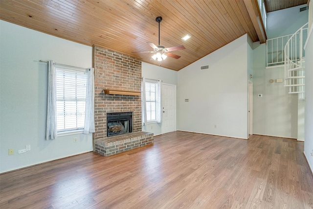 unfurnished living room featuring a brick fireplace, visible vents, lofted ceiling with beams, and wood finished floors