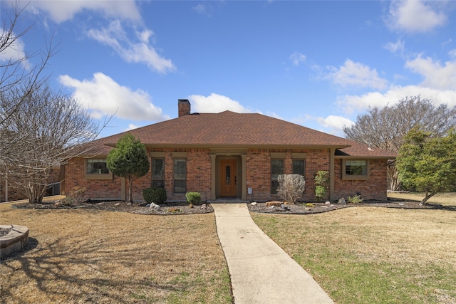 single story home with roof with shingles, brick siding, a chimney, and a front yard