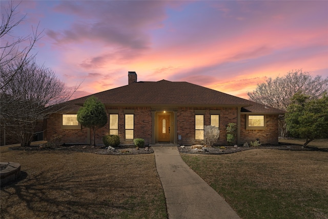 ranch-style home featuring roof with shingles, brick siding, a chimney, and a front yard