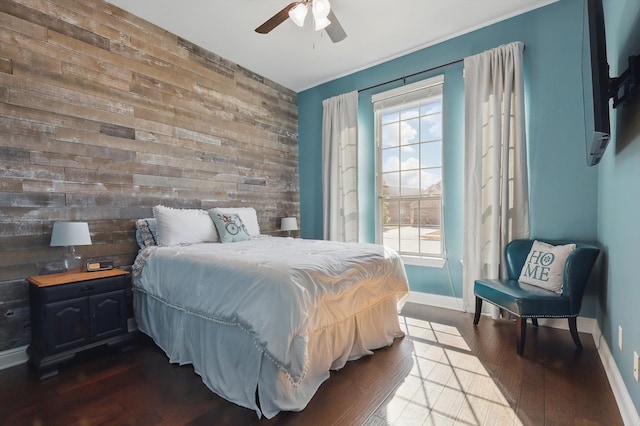 bedroom featuring dark wood-type flooring, ceiling fan, baseboards, an accent wall, and wood walls