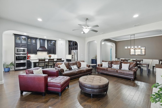 living area with ornamental molding, ceiling fan with notable chandelier, dark wood finished floors, recessed lighting, and arched walkways