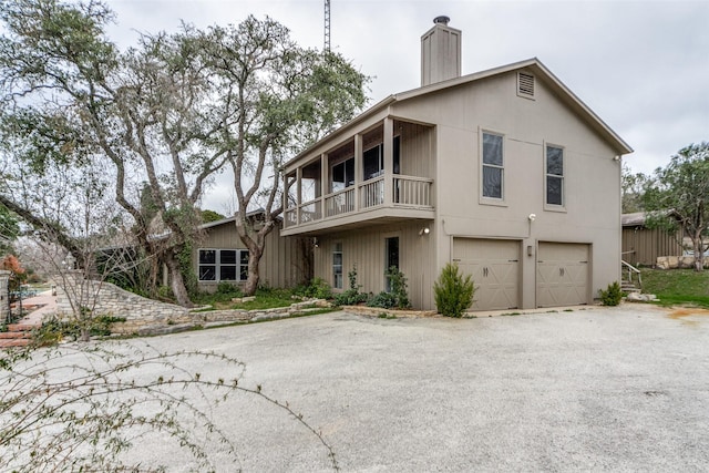 view of front facade featuring aphalt driveway, an attached garage, a chimney, and a balcony