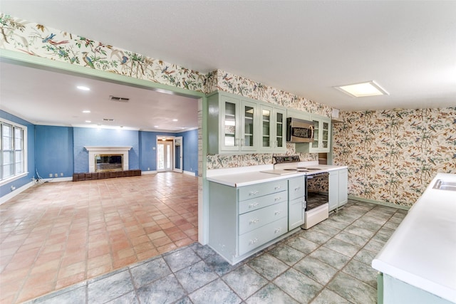 kitchen featuring stainless steel microwave, electric range, a brick fireplace, baseboards, and wallpapered walls