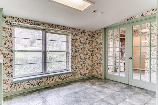 empty room with a wealth of natural light, french doors, baseboards, and wallpapered walls