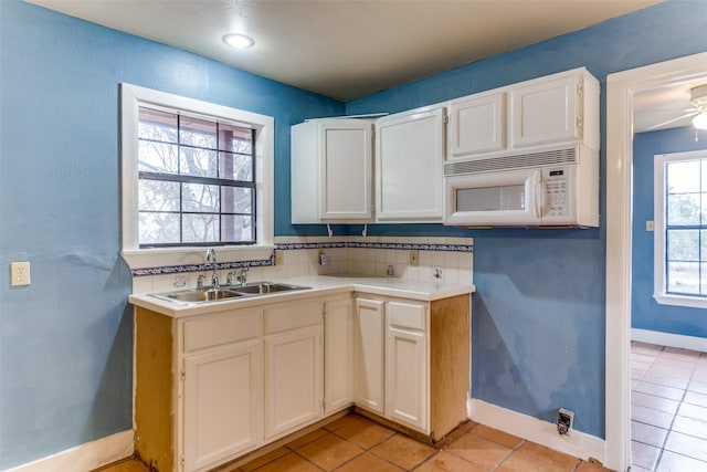 kitchen with light tile patterned floors, light countertops, white microwave, a sink, and baseboards