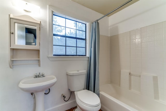 bathroom featuring toilet, baseboards, shower / bath combo with shower curtain, and a sink