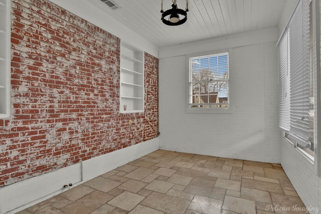 empty room with built in features, brick wall, visible vents, and stone tile flooring