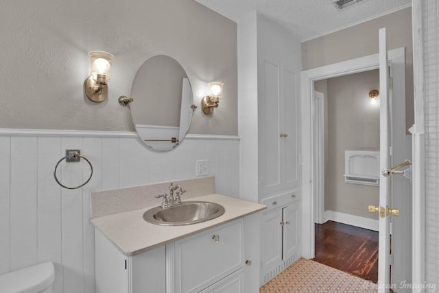 bathroom featuring a textured ceiling, toilet, wood finished floors, vanity, and wainscoting