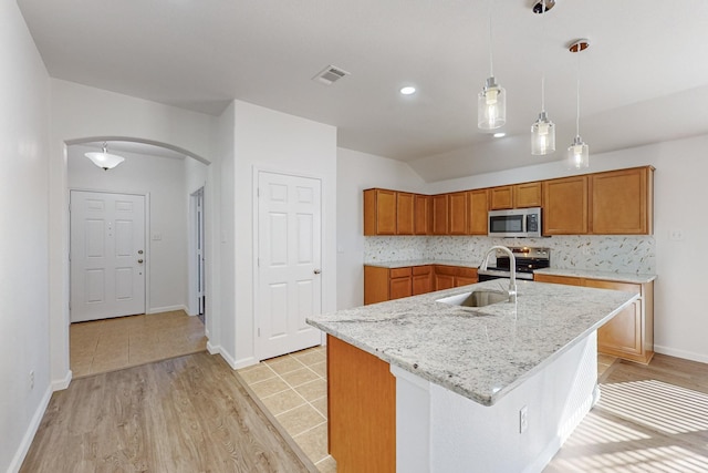 kitchen with arched walkways, lofted ceiling, appliances with stainless steel finishes, brown cabinets, and a sink