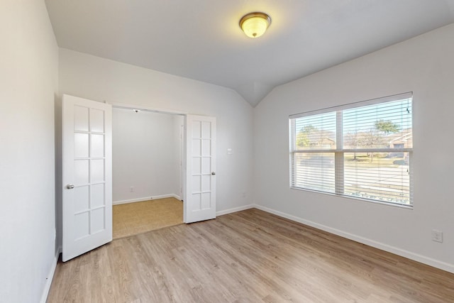 unfurnished bedroom with lofted ceiling, baseboards, and light wood finished floors