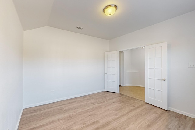 spare room with light wood-style floors, baseboards, visible vents, and vaulted ceiling