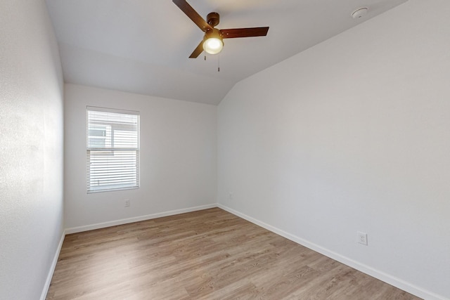 spare room featuring light wood finished floors, baseboards, vaulted ceiling, and a ceiling fan