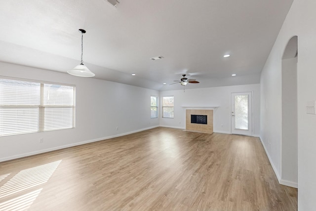 unfurnished living room featuring ceiling fan, light wood-style flooring, visible vents, baseboards, and a tiled fireplace