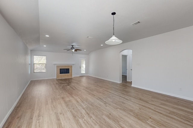 unfurnished living room featuring arched walkways, a fireplace, visible vents, light wood-style floors, and baseboards