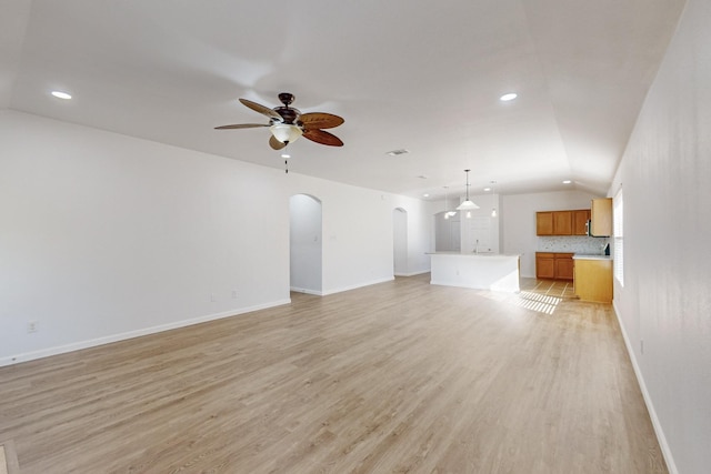 unfurnished living room with arched walkways, ceiling fan, lofted ceiling, light wood-style flooring, and baseboards