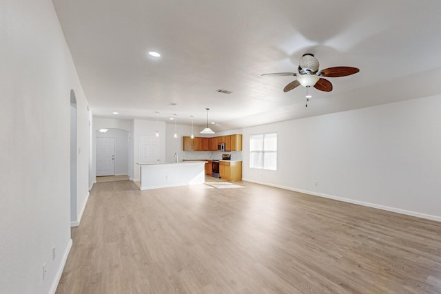 unfurnished living room featuring arched walkways, a ceiling fan, visible vents, baseboards, and light wood finished floors