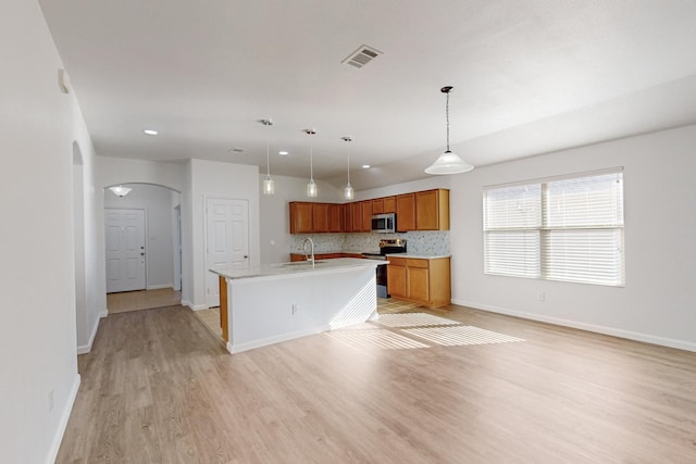 kitchen featuring arched walkways, stainless steel appliances, a sink, visible vents, and brown cabinetry