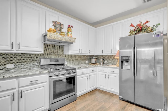 kitchen with light wood-style floors, stainless steel appliances, wall chimney range hood, white cabinetry, and backsplash