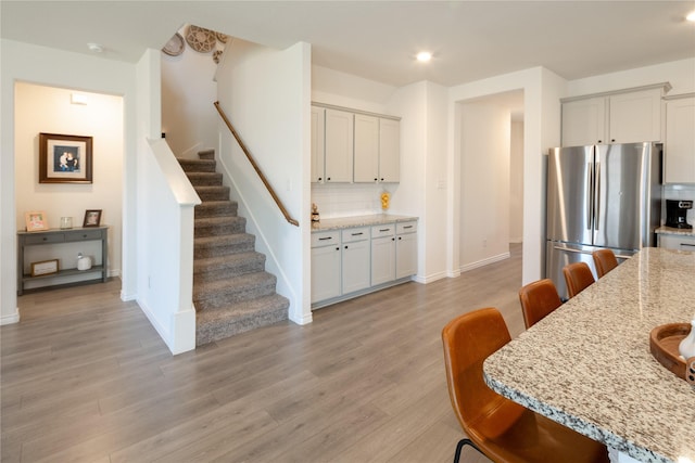 kitchen with a breakfast bar area, tasteful backsplash, light wood-style floors, freestanding refrigerator, and light stone countertops