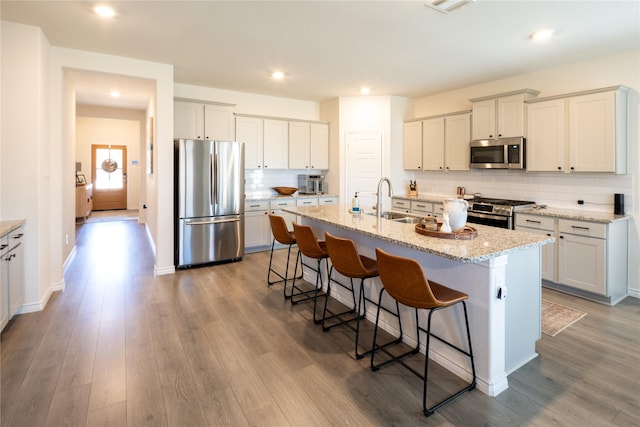 kitchen with a breakfast bar, wood finished floors, a sink, appliances with stainless steel finishes, and backsplash