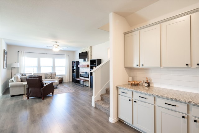 kitchen featuring light stone counters, light wood-style flooring, backsplash, open floor plan, and ceiling fan