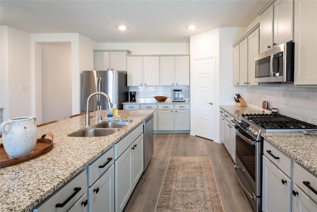 kitchen with tasteful backsplash, appliances with stainless steel finishes, wood finished floors, light stone countertops, and a sink