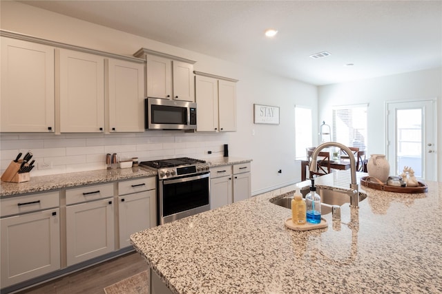 kitchen with dark wood-style flooring, visible vents, backsplash, appliances with stainless steel finishes, and a sink