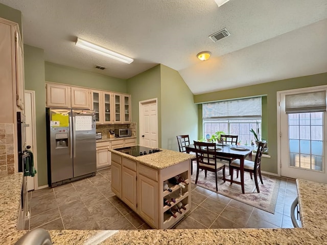 kitchen featuring visible vents, black electric stovetop, glass insert cabinets, and stainless steel refrigerator with ice dispenser