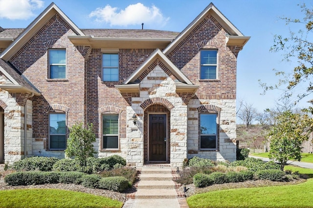 french country style house featuring stone siding, roof with shingles, and brick siding