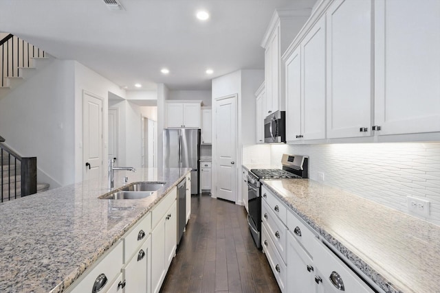 kitchen featuring dark wood-style floors, appliances with stainless steel finishes, a sink, white cabinetry, and backsplash