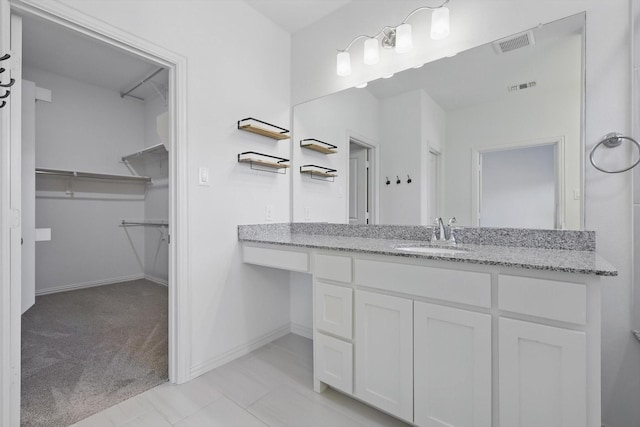 bathroom with a walk in closet, visible vents, vanity, and baseboards