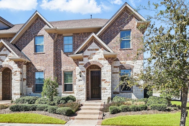 french provincial home with stone siding, roof with shingles, and brick siding