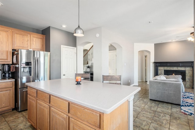 kitchen with a fireplace, a ceiling fan, light countertops, stainless steel refrigerator with ice dispenser, and a center island